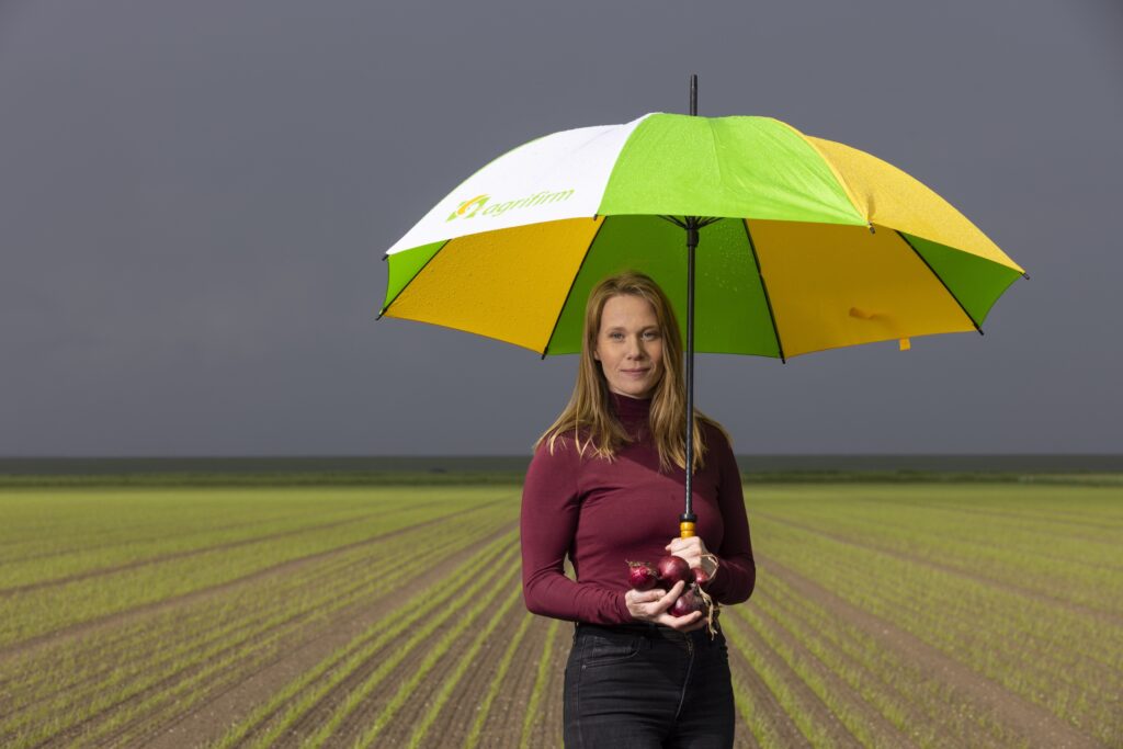 Werkneemster van Agrifirm poseert in akkerland met groen witte paraplu en uien in haar hand