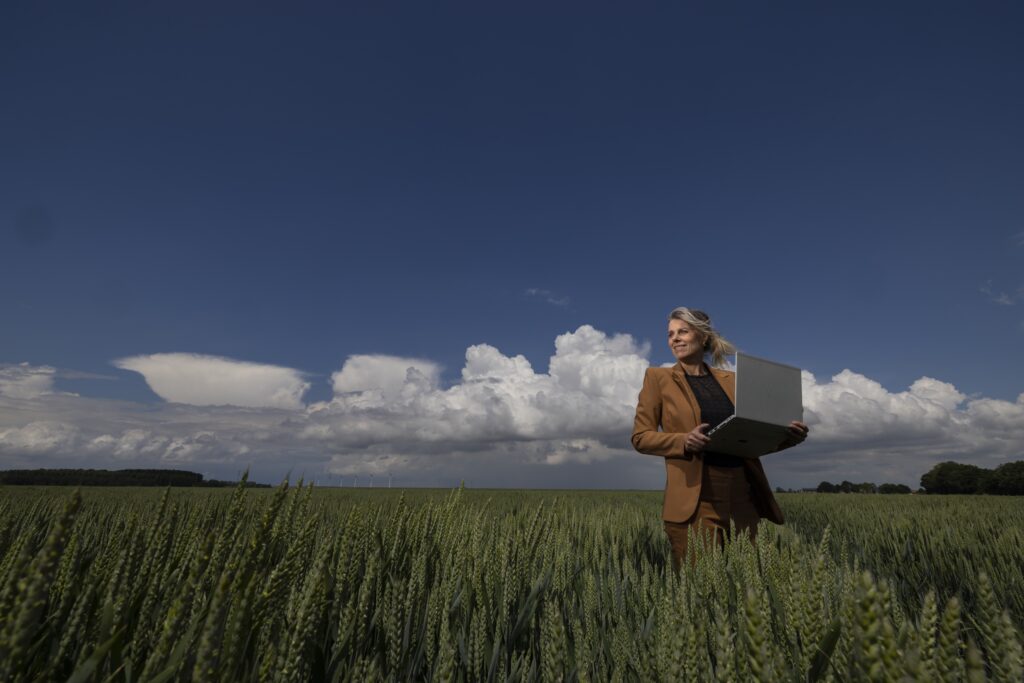 Dame in bruin kostuum staat in tussen de tarwe met een prachtige wolkenlucht in de achtergrond
