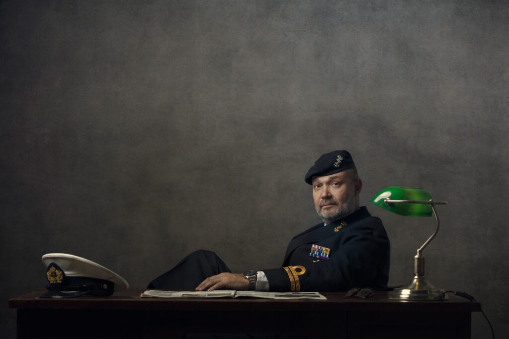 Sfeer portret van een man in een Chesterffield stoel in Peaky Blinders stijl die een glas whiskey vast houdt.