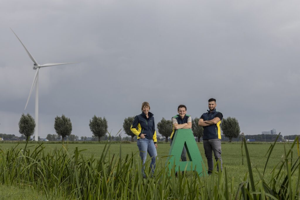 Drie mederwerkers van Agrifirm poseren in een weiland op de letter A, van Agrifirm, met een rietkraag in de voorgrond