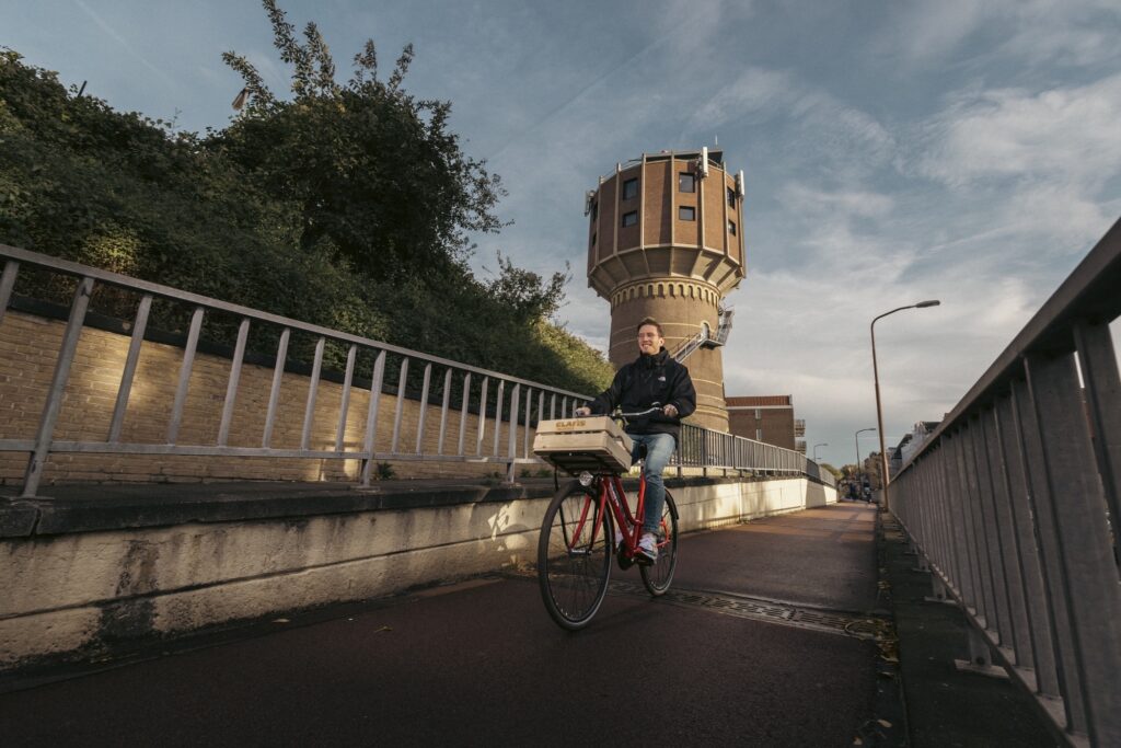 Werknemer van Clafis fiets op een rode fiets met voorop een krat voor hun bijzondere kantoor, een watertoren, langs.