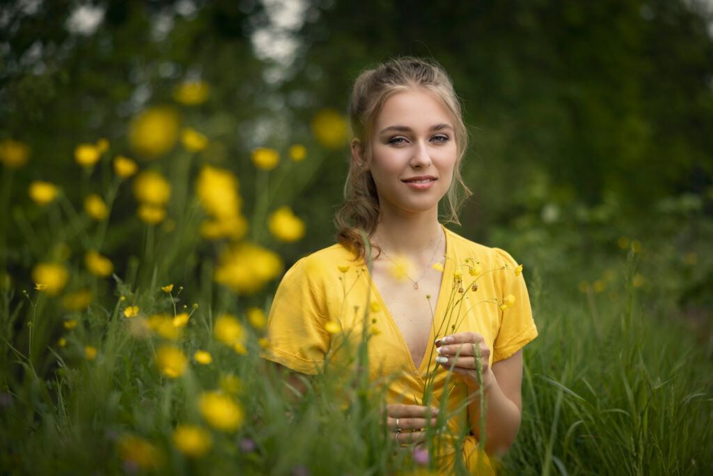 jonge dame gekleed in zomerse gele jurk zit in het hoge gras met gele bloemen in de voorgrond