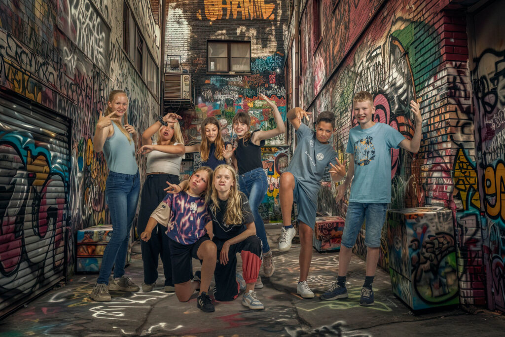 9 kinderen van de basisschool staan vrolijk in een steeg met veel graffiti op de muren