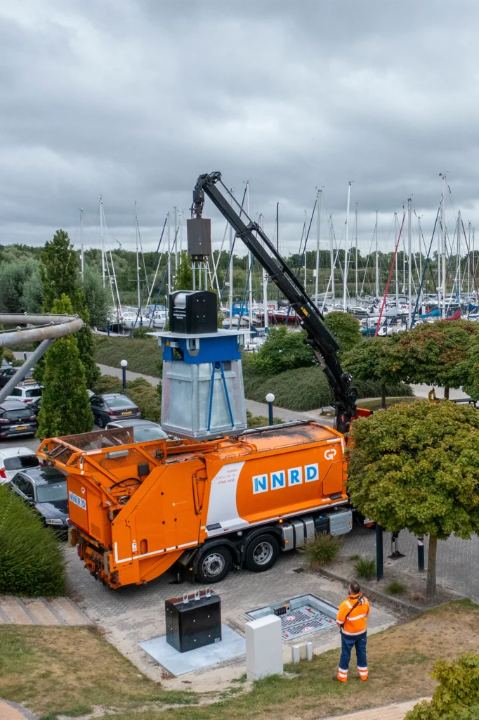 Drone foto van een oranje vuilniswagen van NNRD die net geleegd wordt