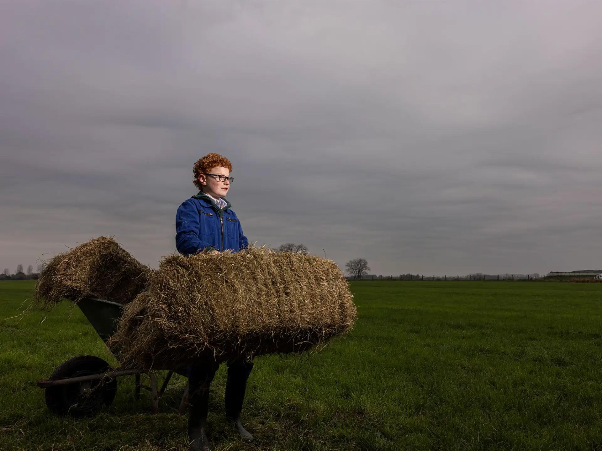 Boerenzoon in blauwe overall staat met een hooibaal in zijn handen