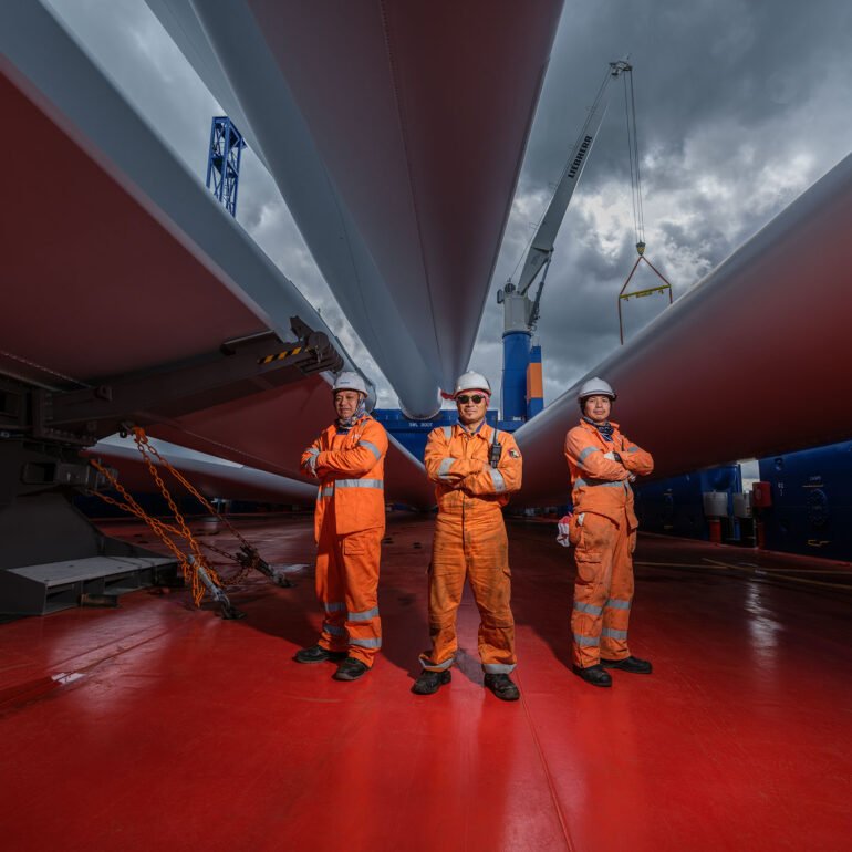 Personeel poseert op dek van schip onder grote onderdelen van windmolen