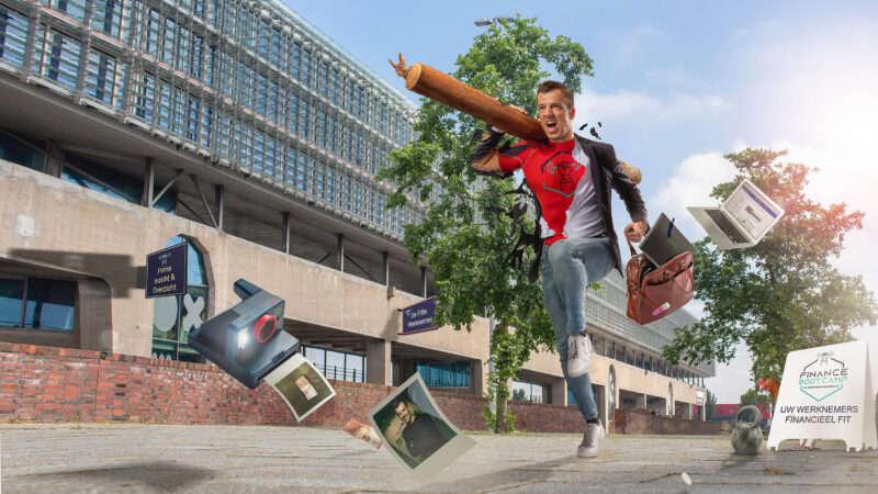 Man met een boomstam op zijn schouder springt voor een modern gebouw, tussen zwevende voorwerpen.