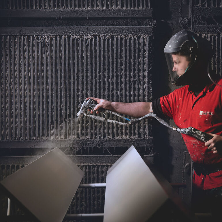 Medewerker met gelaatsbescherming spuit hangende metalen panelen in een spuitcabine