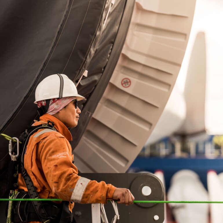 Medewerker met veiligheidshelm en veiligheidsharnas staat naast een groot industrieel onderdeel aan boord