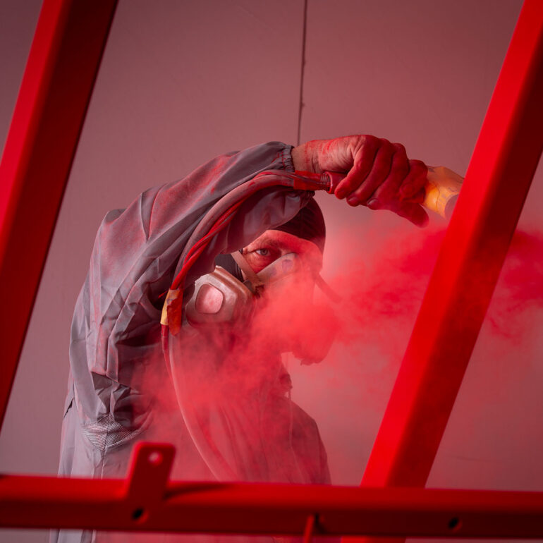 Poedercoater met adembescherming spuit de bovenkant van een rood metalen frame