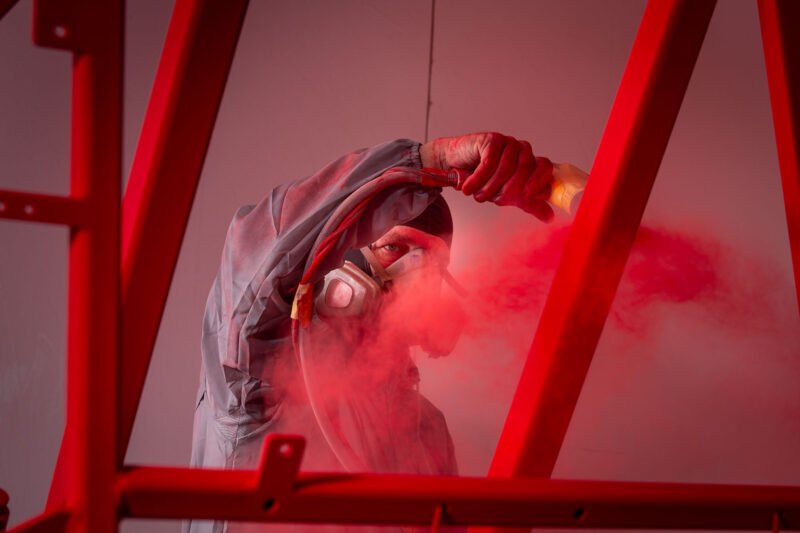 Poedercoater met adembescherming spuit de bovenkant van een rood metalen frame