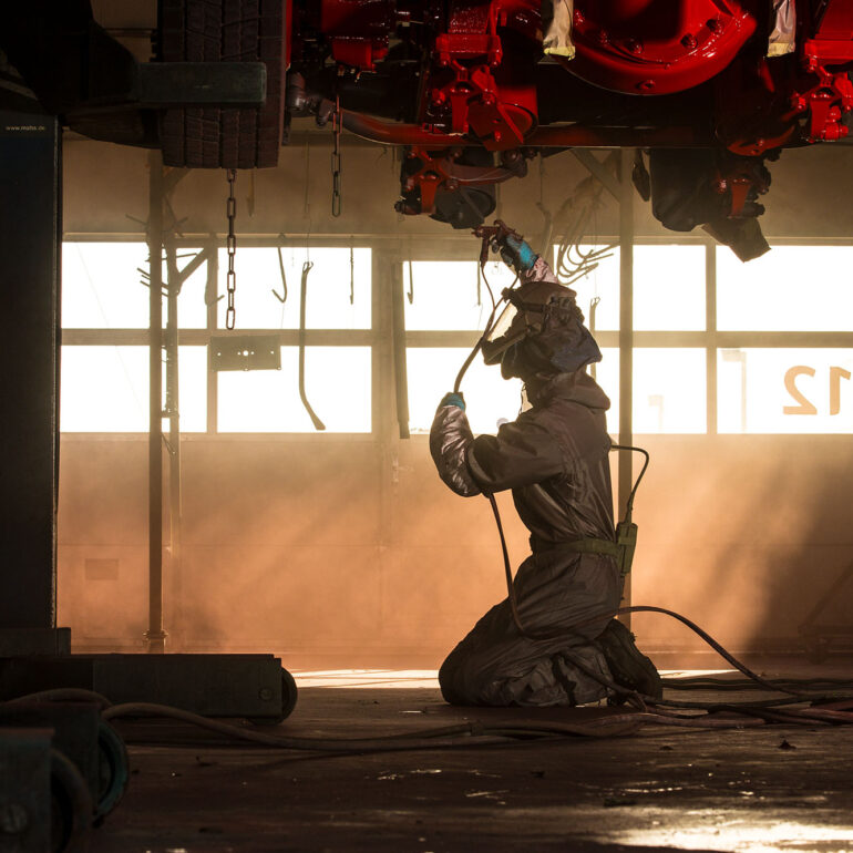 Medewerker in beschermende kleding spuit de onderzijde van een machine in een werkplaats