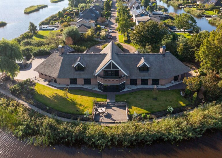 Luchtfoto van een villa met rieten dak, terras en tuin aan het water