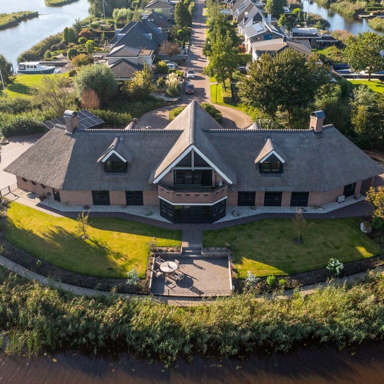 Luchtfoto van een villa met rieten dak, terras en tuin aan het water