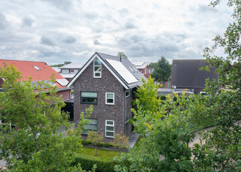 Verhoogd zicht op een vrijstaande woning met zonnepanelen, tuin en omliggende huizen