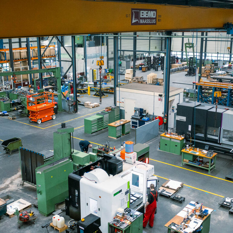 Overzicht van een productiehal met metaalbewerkingsmachines, een bovenloopkraan en medewerkers