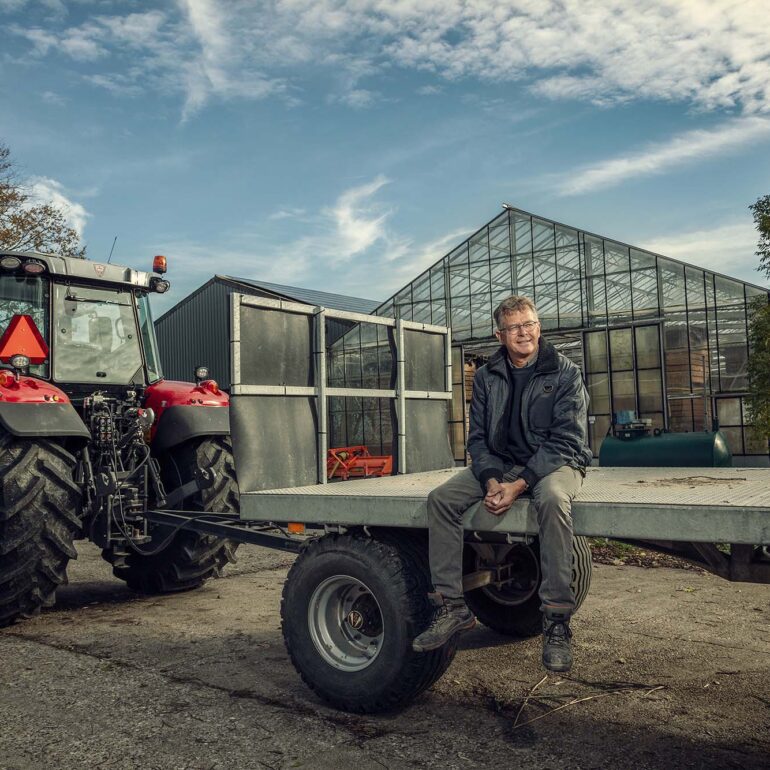 Boer zit op de aanhanger die achter zijn rode tractor gekoppeld is.