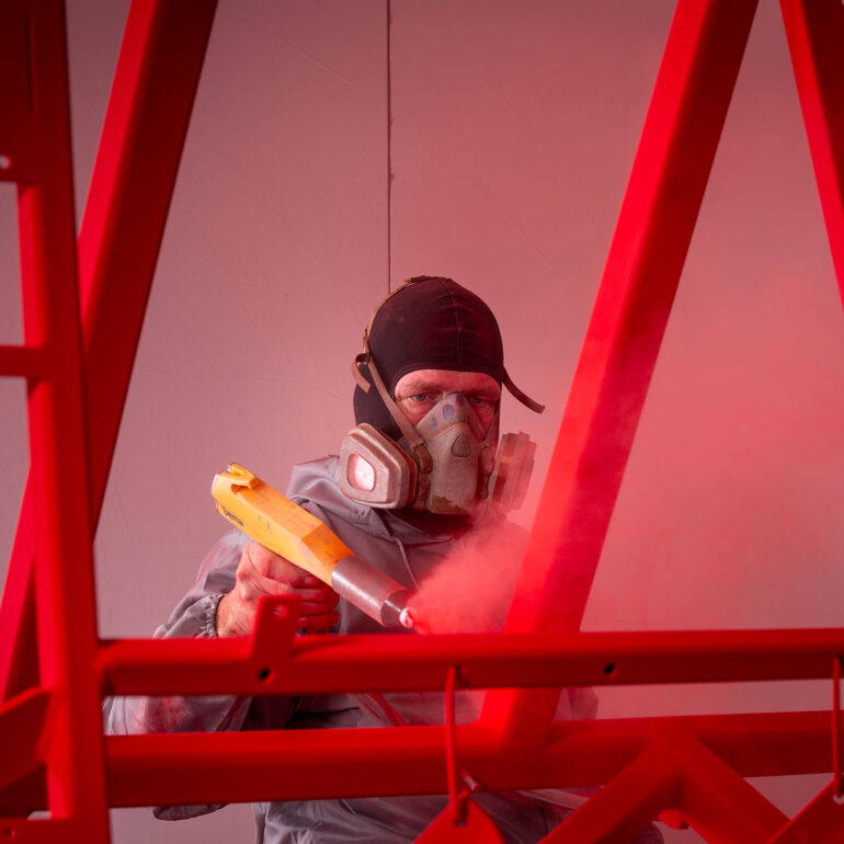 Poedercoater met adembescherming brengt een rode coating aan op een metalen frame