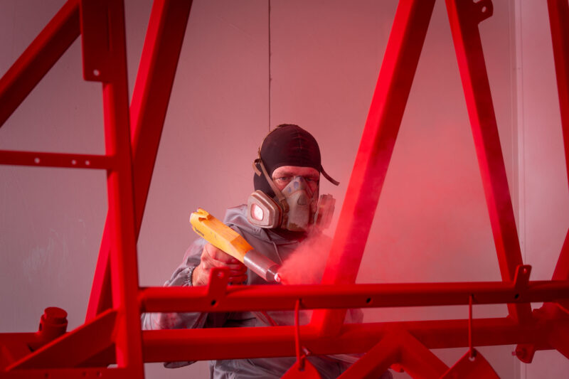 Poedercoater met adembescherming brengt een rode coating aan op een metalen frame