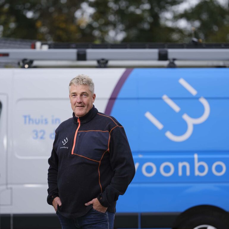 Mederwerker van woonorganisatie staat voor blauwe bus