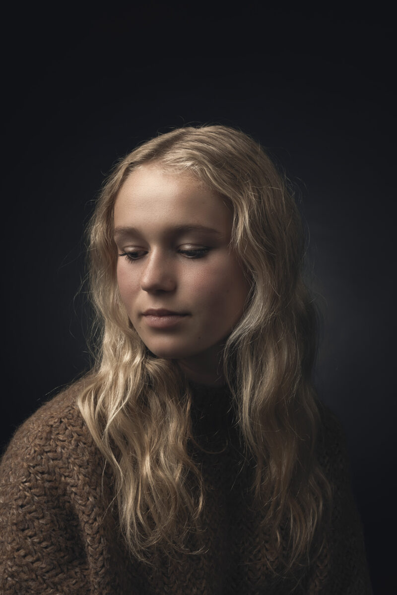 Portret van een meisje met lang blond haar en een bruine trui.