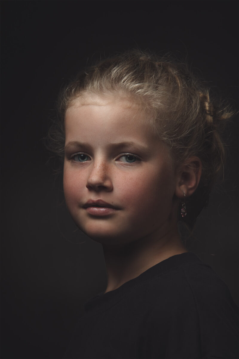 Fine-art portret van een meisje met haar opgestoken tegen een donkere achtergrond.