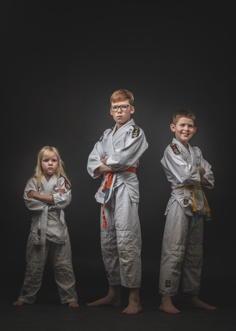 Portret van drie kinderen in judopakken tegen een donkere achtergrond.