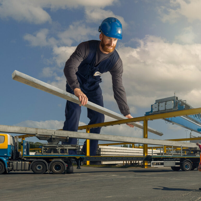 Fotomontage van een reusachtige medewerker met veiligheidshelm die een betonnen balk boven een vrachtwagen houdt