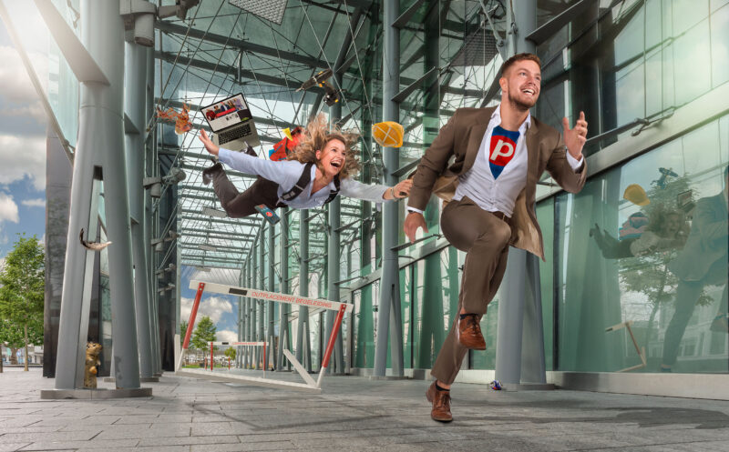 Man in pak en een zwevende vrouw bewegen door een glazen atrium, omringd door losse voorwerpen.