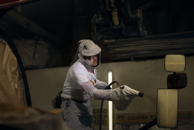 Medewerker in een witte beschermende overall houdt spuitapparatuur vast in de werkplaats