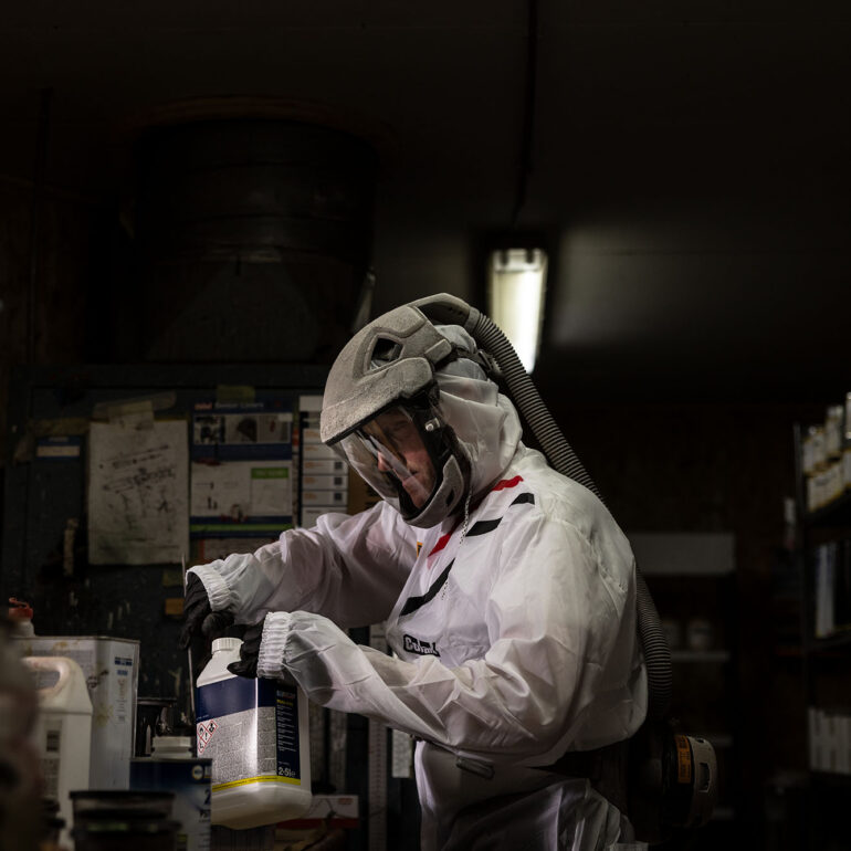 Medewerker met beschermende kap werkt met een container coatingmateriaal in de werkplaats