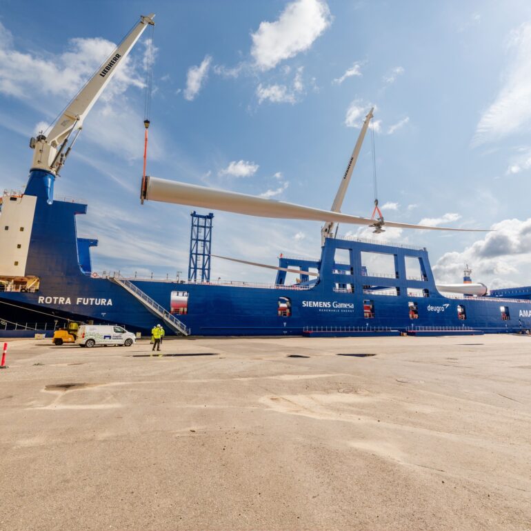 Havenkranen hijsen een lang windturbineblad boven het vrachtschip Rotra Futura