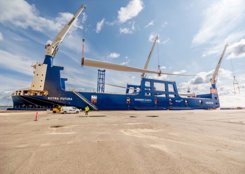 Havenkranen hijsen een lang windturbineblad boven het vrachtschip Rotra Futura