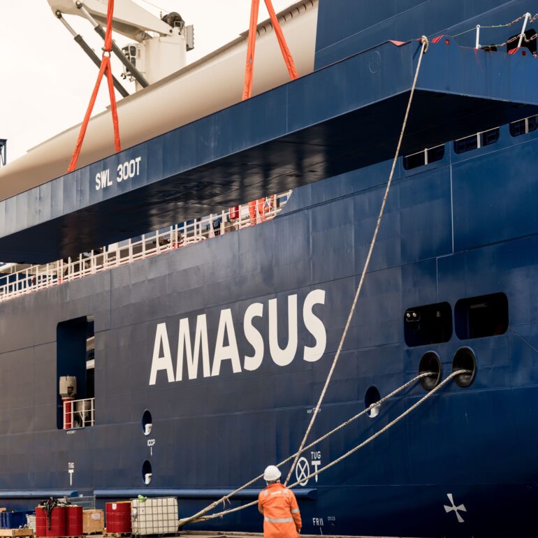 Medewerker in oranje werkkleding staat op de kade naast een blauw Amasus-schip