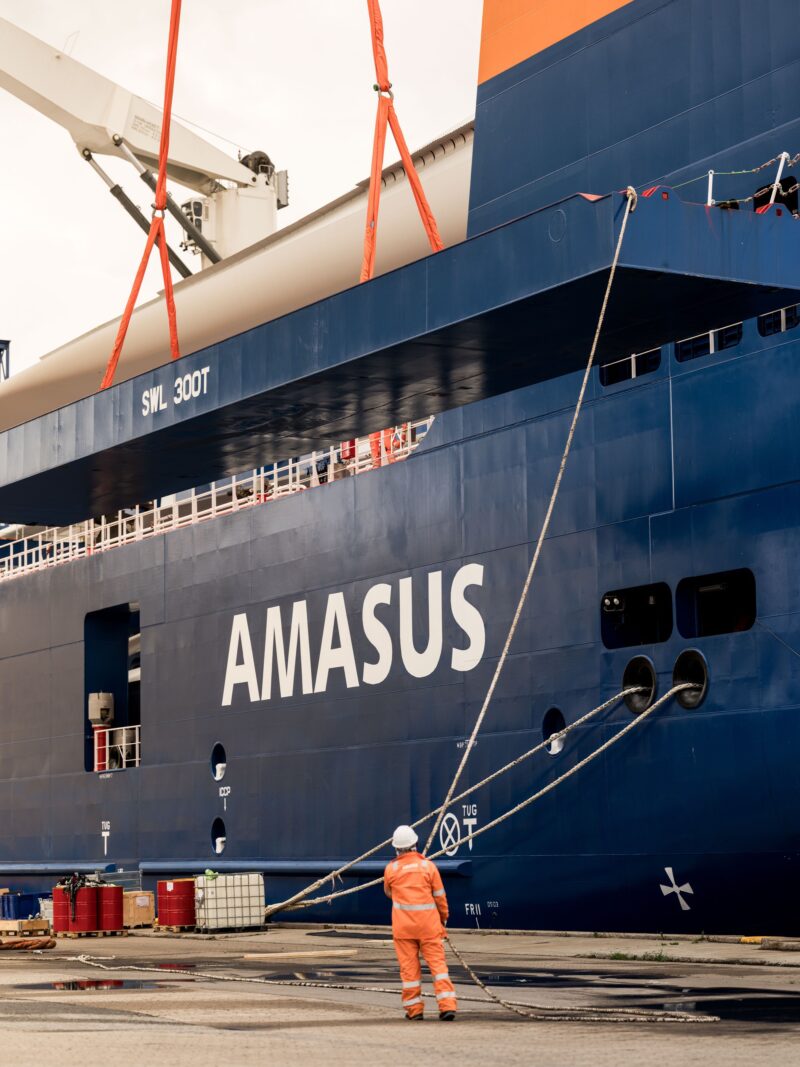 Medewerker in oranje werkkleding staat op de kade naast een blauw Amasus-schip
