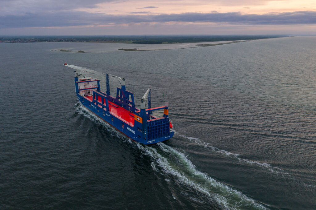 Dronefoto van een varend vrachtschip met een lang schuimspoor en de kust op de achtergrond