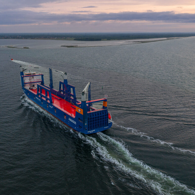 Dronefoto van een varend vrachtschip met een lang schuimspoor en de kust op de achtergrond