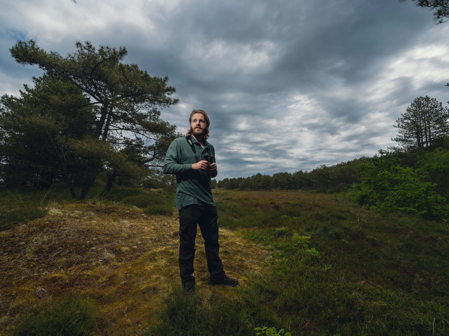 Boswachter Vlieland staat met verrekijker voor heide grond