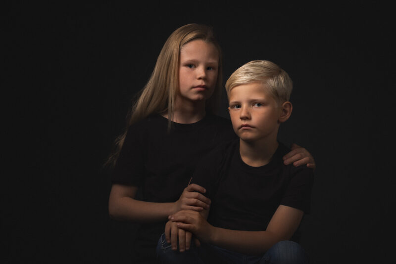 Studioportret van een jongen en een meisje tegen een donkere achtergrond.