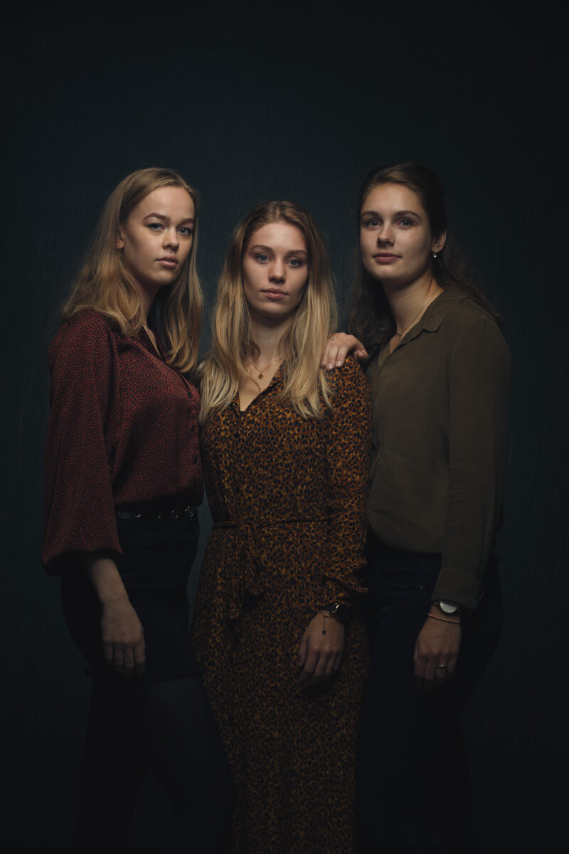 Portret van drie zussen die naast elkaar staan tegen een donkere achtergrond.