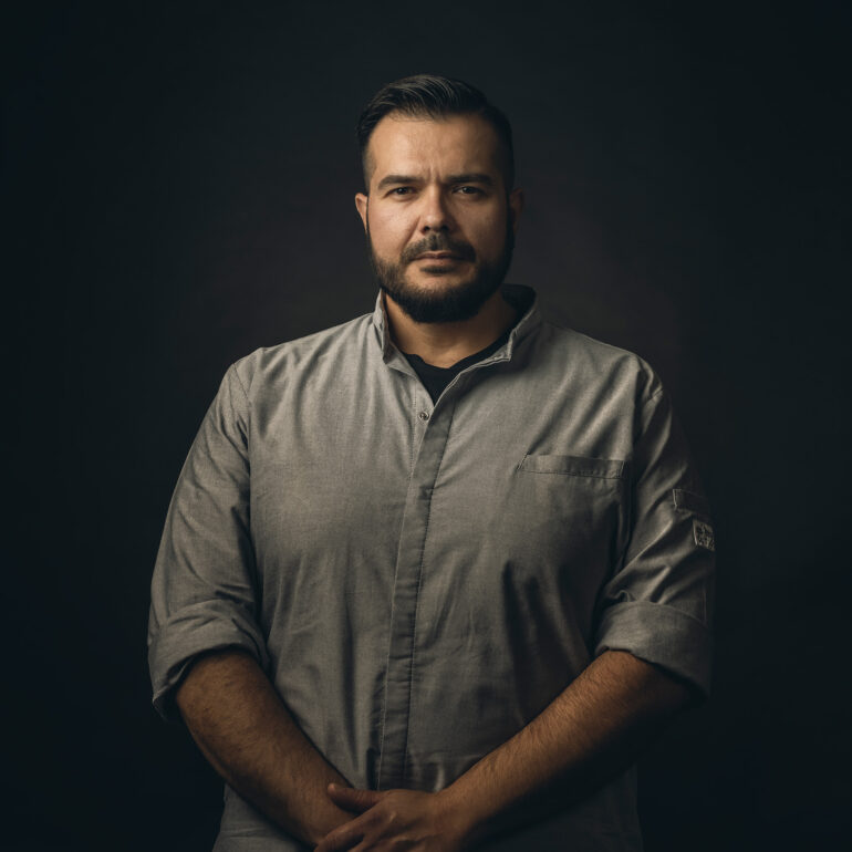 Portret van een man met een donkere koksjas tegen een donkere achtergrond.