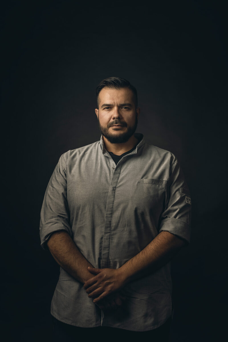 Portret van een man met een donkere koksjas tegen een donkere achtergrond.