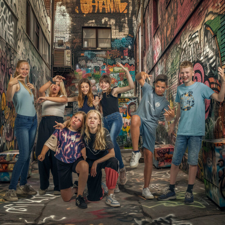 Groep kinderen poseert speels in een smalle steeg met kleurrijke graffiti.