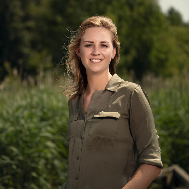 Lachende vrouw in een olijfgroene blouse staat buiten tussen het groen.