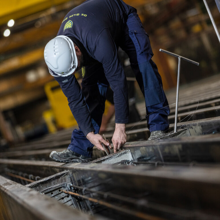 Medewerker met veiligheidshelm werkt aan wapening in een lange productiemal in een fabriekshal