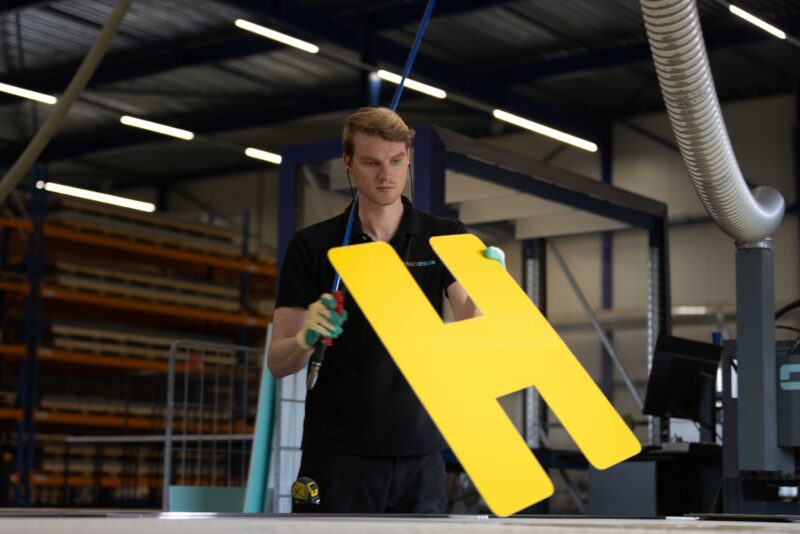 Panelvision-medewerker houdt een geel uitgefreesd onderdeel vast in de werkplaats.