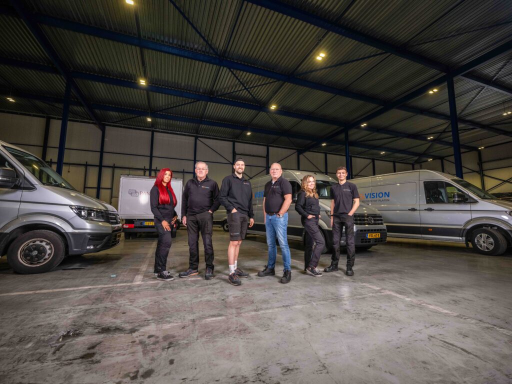 Panelvision-medewerkers staan samen tussen bedrijfswagens in een bedrijfshal.