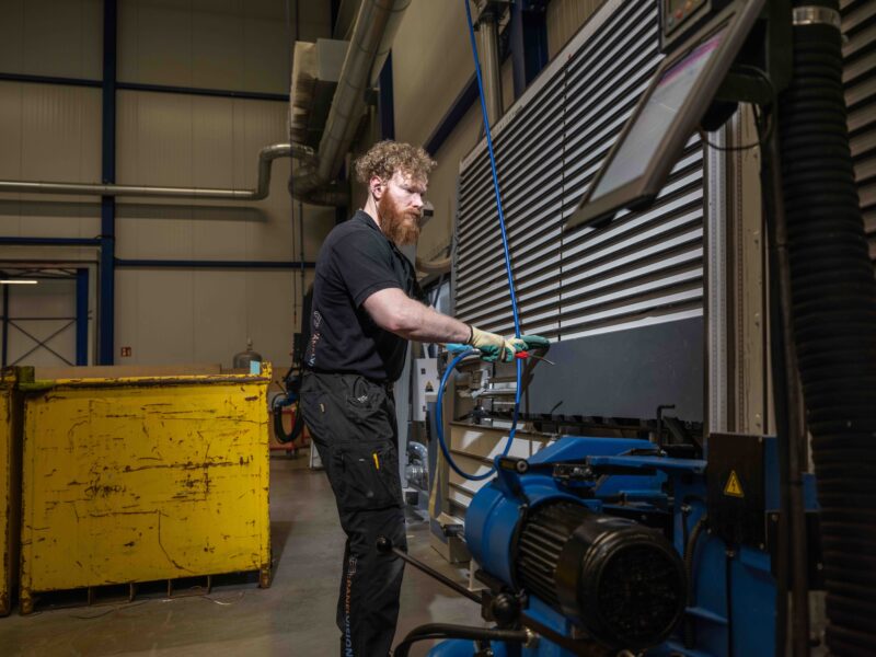 Panelvision-medewerker in zwarte bedrijfskleding werkt bij een grote plaatbewerkingsmachine.