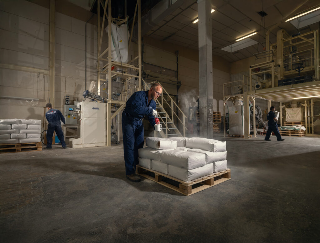 Wymenga-medewerkers werken tussen installaties en pallets met zakken in de productiehal in Wergea.
