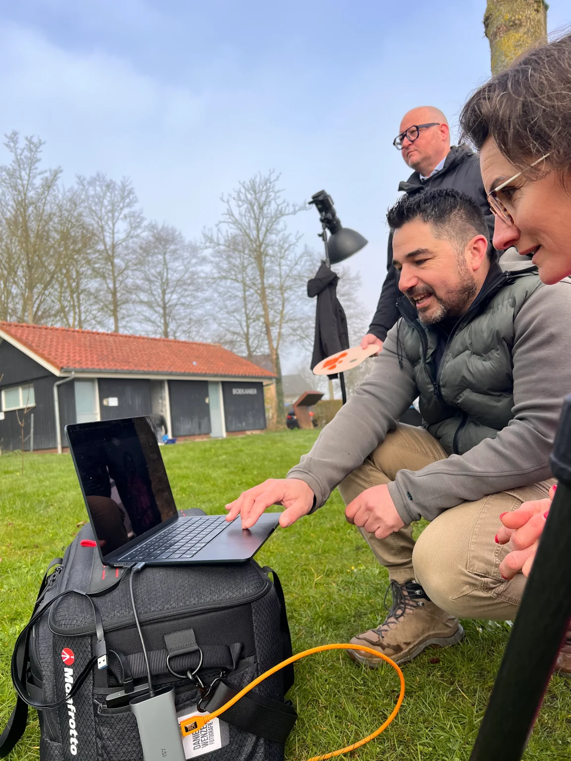 Fotograaf en twee andere personen bekijken buiten de beelden op een laptop.